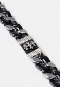 Pulseira de corrente preta e prateada com elos interligados, apresentando um centro retangular com um padrão texturizado e um detalhe metálico decorativo.