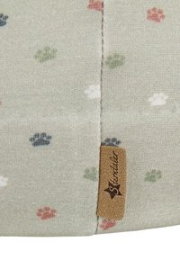 Close-up of beige fabric with multicolored paw prints and a brown stitched Sterntaler brand label on a seam.
