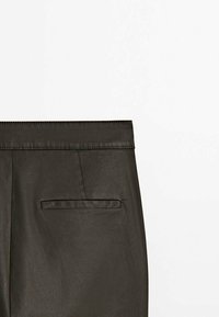 Pantalon en simili cuir noir avec une texture lisse, une ceinture plate et une seule poche arrière avec une ouverture rectangulaire.