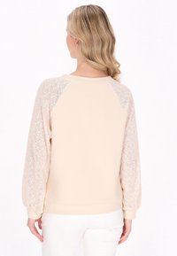 Felpa beige chiaro con maniche in pizzo texture e scollatura rotonda, corpo liscio e orlo a coste per un look aderente.