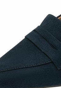 Mocassin en daim bleu marine avec une bride pour pièce et des coutures détaillées sur la partie supérieure de la chaussure.