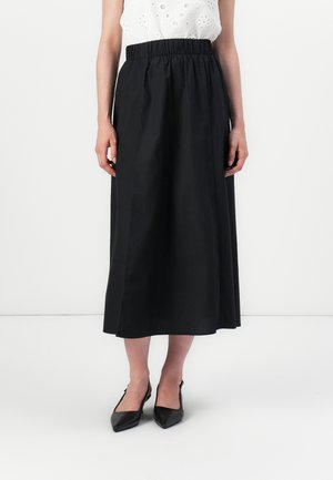 A person is wearing a black, knee-length skirt and pointed black heels, standing against a white background. The top is white and embroidered.