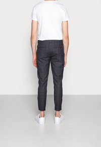 Donker geruite broek met een slim fit, gemaakt van zachte stof, met een platte voorkant en twee achterzakken, gecombineerd met een wit T-shirt en witte sneakers.