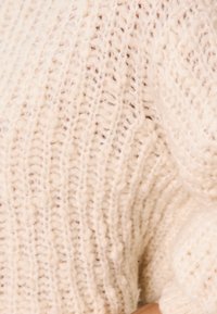 Maglione lavorato a maglia in morbido filato color crema, caratterizzato da una texture a coste e un'intrecciatura morbida. Dettagliato con una vestibilità leggermente sovradimensionata per il massimo comfort.