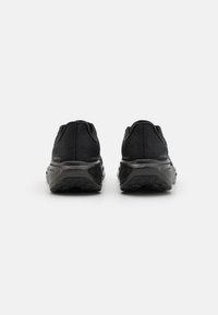 Baskets de sport noires avec une tige en mesh texturé, un col rembourré et une semelle en caoutchouc dotée d'un motif de traction multidirectionnel.