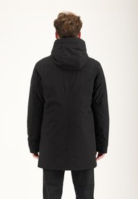 Parka nera con cappuccio, dalla superficie liscia, di lunghezza estesa e con un delicato dettaglio delle cuciture che corre verticalmente lungo la schiena.