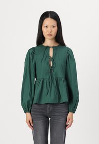 Blusa de algodão verde com mangas bufantes, decote redondo e detalhe de laço frontal. Apresenta cintura franzida e um ajuste solto.