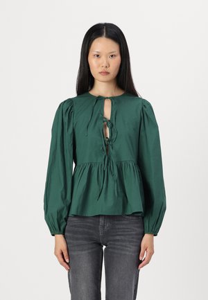 Blusa in cotone verde con maniche a palloncino, scollatura rotonda e dettaglio con fiocco sul davanti. Presenta una vita arricciata e una vestibilità morbida.