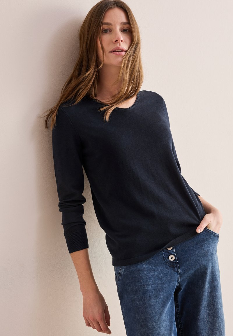 Marineblauwe trui met lange mouwen en een ronde halslijn, zachte textuur en geribbelde manchetten, gecombineerd met lichtblauwe jeans met een relaxte pasvorm en knoopdetails.