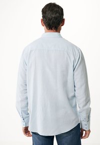 Camisa de manga larga azul claro con cuello estándar, puños de botón y yugo trasero, que presenta una textura suave y un corte holgado.