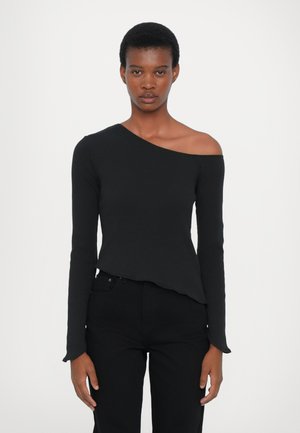 Black asymmetrical long-sleeve top with one shoulder exposed, featuring a fitted design and soft texture, paired with black jeans.