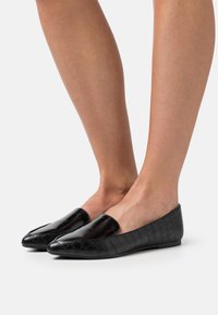 Černé ploché boty s elegantním, lesklým svrškem a krokodýlí strukturou na bocích. Nízký profil a špičatý design špičky.