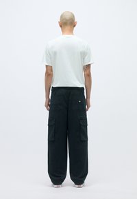 Υπερμεγέθες μαύρο cargo παντελόνι με μεγάλες τσέπες, συνδυασμένο με εφαρμοστό λευκό μπλουζάκι. Λείος ύφασμα και χαλαρή σιλουέτα.