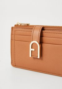 Brown leather wallet featuring a gold zipper, a gold accent hardware with an outlined letter “A,” and multiple card slots on one side.
