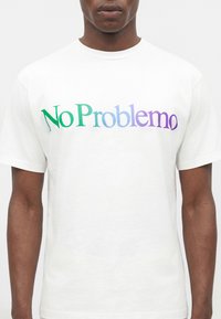 Άνδρας που φοράει λευκό T-shirt με το κείμενο «No Problemo» σε πράσινο προς μοβ διαβάθμιση στο στήθος.