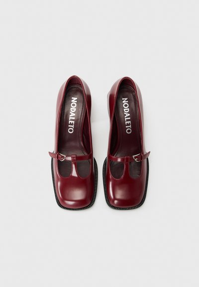 Chaussures Mary Jane en cuir bourgogne avec un bout rond, des détails découpés transparents, une sangle réglable et une semelle noire texturée.