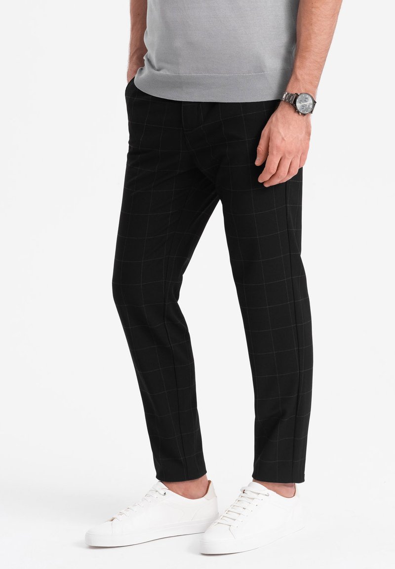 Pantalon à carreaux noirs avec une coupe slim, en tissu doux. Assorti à des baskets blanches ; détails discrets à la taille et design épuré.