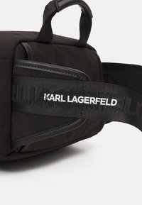 Borsa nera di tessuto con forma strutturata, dotata di una cintura testurizzata con "KARL LAGERFELD" in bianco. Superficie liscia e materiale resistente.