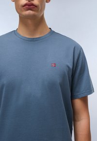 T-shirt en coton bleu à manches courtes, col rond, avec un petit drapeau norvégien brodé sur la poitrine gauche. Texture douce et lisse.