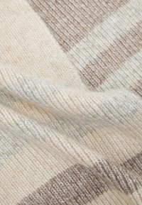 Tissu tricoté dans des tons crème et marron clair, présentant un mélange de rayures et de textures, avec un aspect doux et légèrement duveteux.