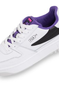 Sneaker bianco con accenti neri e viola, caratterizzato da una tomaia in pelle texture, lacci piatti e una colleretta imbottita per la caviglia con dettaglio del logo.