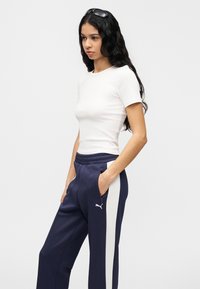 Λευκό εφαρμοστό T-shirt και ναυτικό μπλε φόρμα με λευκές κάθετες ρίγες στα πλάγια. Η φόρμα έχει ελαστική μέση και τσέπες. Χωρίς εμφανή λογότυπα.