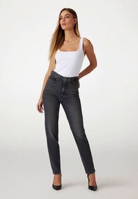 Magas derekú, sötét színű farmernadrág, karcsúsított szabású és enyhén rugalmas, fehér, testhezálló trikóval és fekete magas sarkú cipővel párosítva.