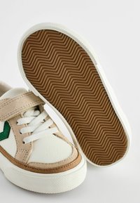 Weiße Leder- und beige Wildledersneaker mit grünen Akzenten, flacher Gummisohle mit Fischgrätenmuster und weißen Schnürsenkeln.