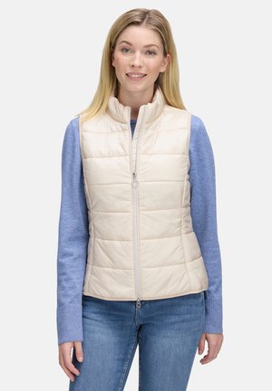 Beige Steppweste mit Stehkragen, Reißverschluss und horizontalem Steppmuster. Trägt man über einem blauen Langarmshirt, kombiniert mit Jeans.