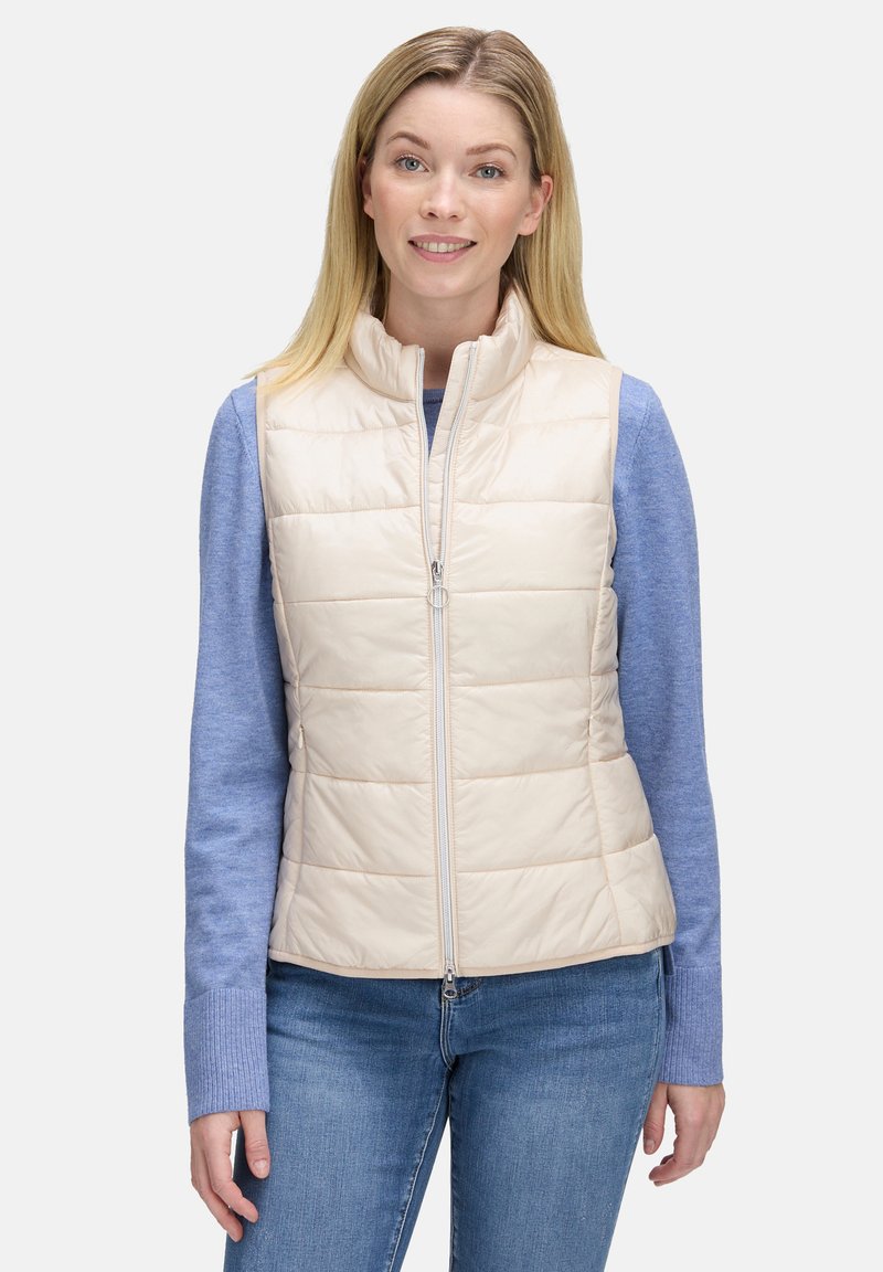 Beżowa kamizelka puchowa z kołnierzem stojącym, z zamkiem błyskawicznym oraz poziomym pikowaniem. Nosi ją osoba na niebieskiej koszuli z długim rękawem, zestawiona z dżinsami.