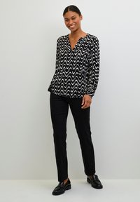 Blusa a zigzag in bianco e nero con scollatura a V e maniche lunghe, abbinata a pantaloni neri aderenti e scarpe slip-on nere.