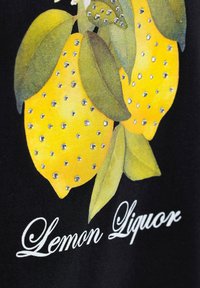 Tela negra con un vibrante gráfico de dos limones amarillos con hojas verdes, adornada con strass plateados y texto blanco que dice "Limonada Licor".