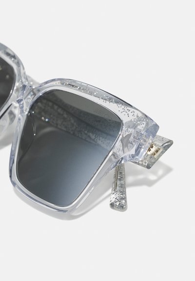 Ochelari de soare supradimensionați, transparenți, cu accente de sclipici argintiu, lentile întunecate și o ramă texturată clară, dotată cu accesorii aurii.