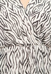 Un tissu à motif zèbre noir et blanc présente un design enveloppant avec une taille froncée. Texture douce avec un aspect lisse et fluide.