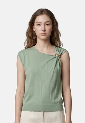 Giovane donna con capelli mossi che indossa un top verde chiaro senza maniche con un dettaglio arricciato sulla spalla fissato da una fibbia dorata.