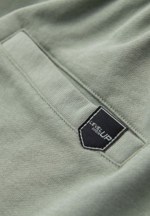 Close-up of light green fabric pocket with black rectangular label reading "LEVEL UP" stitched near the edge.