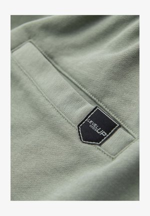 Close-up of light green fabric pocket with black rectangular label reading "LEVEL UP" stitched near the edge.