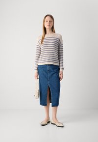 Gebreide trui in crèmekleur met lichtblauwe strepen, gecombineerd met een blauwe denimrok met een split aan de voorkant, en beige platte schoenen.