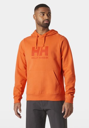 Sudadera de algodón naranja con bolsillo tipo canguro, capucha con cordón y gran logo rojo de Helly Hansen en el frente. Textura suave y diseño ajustado.