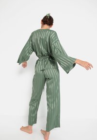 Groen satijnen loungewear set met brede mouwen, een ceintuur om de taille en verticale strepen op zowel de top als de broek. Gladde textuur.