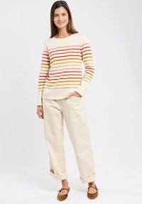 Cremefarvet langærmet bluse med vandrette striber i rød, orange og gul. Sammen med lysebeige bukser og brune flade sko.