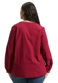 Burgunderfarbige Bluse mit langen Ärmeln aus strukturiertem Stoff, Rundhalsausschnitt, lockerer Passform und geknöpften Manschetten. Die Rückansicht zeigt den lässigen Stil.