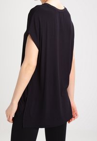 Černé oversized tričko s krátkými rukávy, kulatým výstřihem a bočními rozparky pro snadný pohyb. Vyrobeno z měkké, lehké látky.