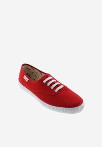 Zapatilla de lona roja con suela de goma blanca, que cuenta con cordones blancos y una etiqueta de logo en el lateral. Textura suave con diseño de punta redondeada.