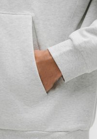 Lys grå sweatshirt med en stor frontlomme, ribbede manchetter og glat tekstur. Har et lille logo detajle på stoffet.