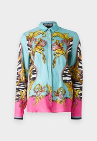 Camicia di seta turchese, con ornate strisce a zigzag dorate e nere. Accentuata da dettagli rosa all'orlo e nelle maniche, con motivi intricati.