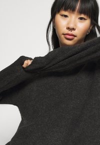 Dunkelgrauer, oversized Pullover aus geripptem Material mit langen Ärmeln und luftigem Schnitt. Der Stoff wirkt weich und warm.