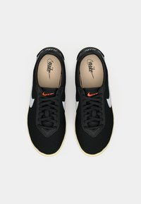 Μαύρα αθλητικά παπούτσια με επάνω μέρος από δίχτυ, λευκό λογότυπο Swoosh, μαύρες κορδόνες, πορτοκαλί λεπτομέρειες και σόλα από καουτσούκ σε ελεφαντόδοντο.