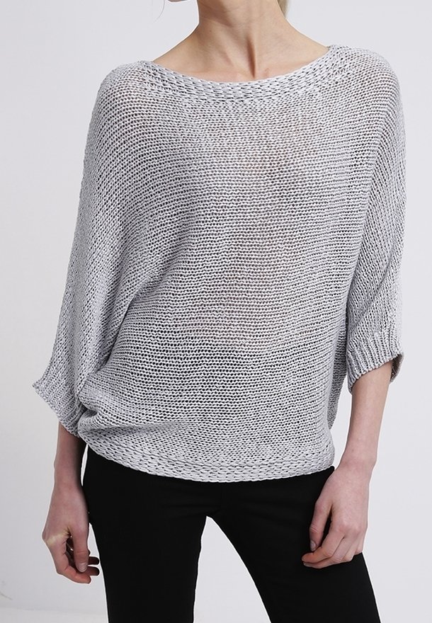 Hellgrauer, oversized Strickpullover mit lockerem Gewebe, weitem Ausschnitt und Dreiviertelärmeln. Kombiniert mit schwarzen, eng anliegenden Hosen.