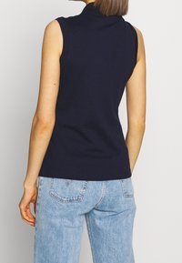 Marinblus utan ärmar med hög krage, tillverkad av mjukt tyg; kombinerad med ljusblå denimjeans med bakfickor och en lätt tvätt.